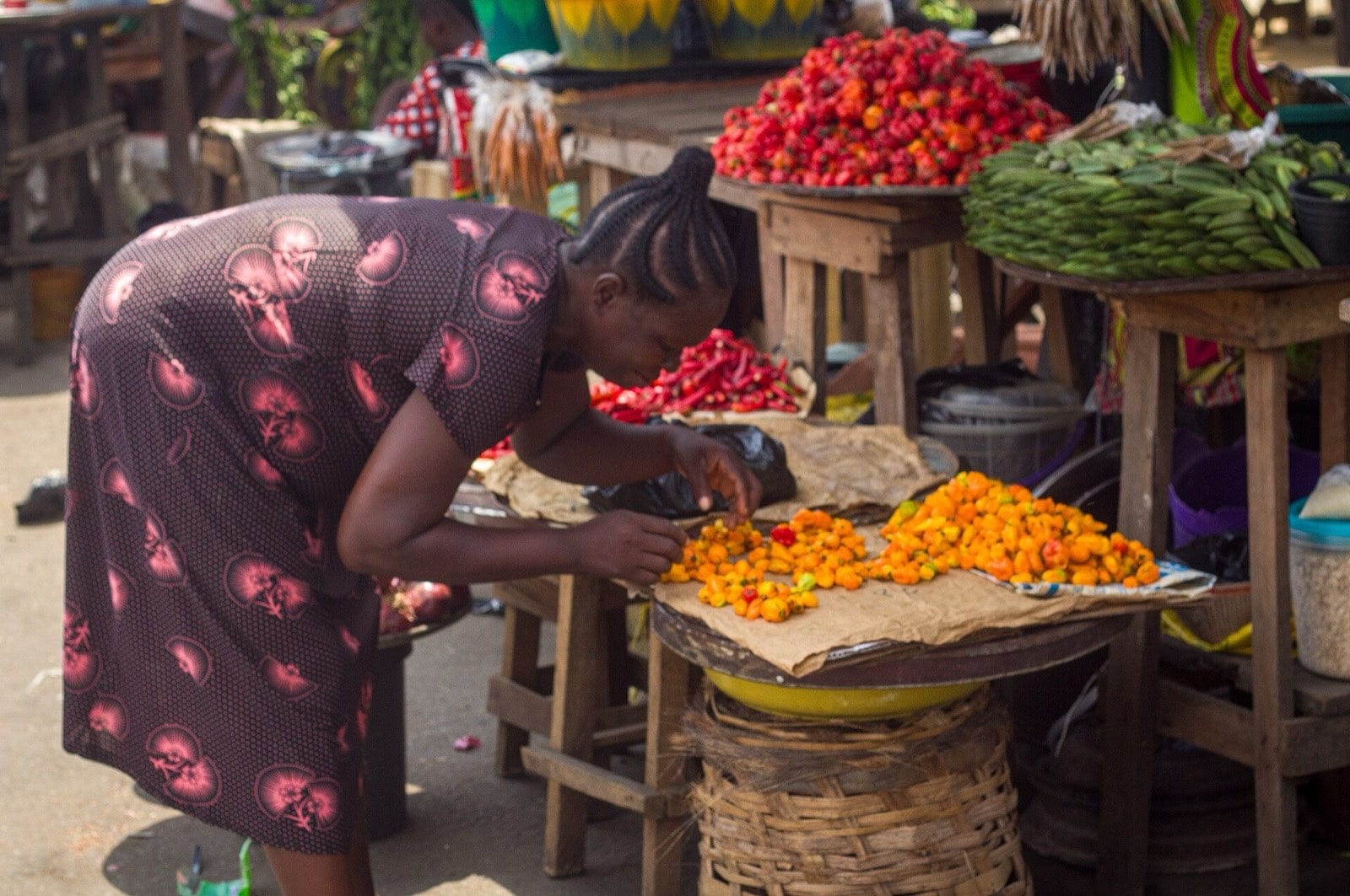 A woman arranging fresh peppers on a market stall.