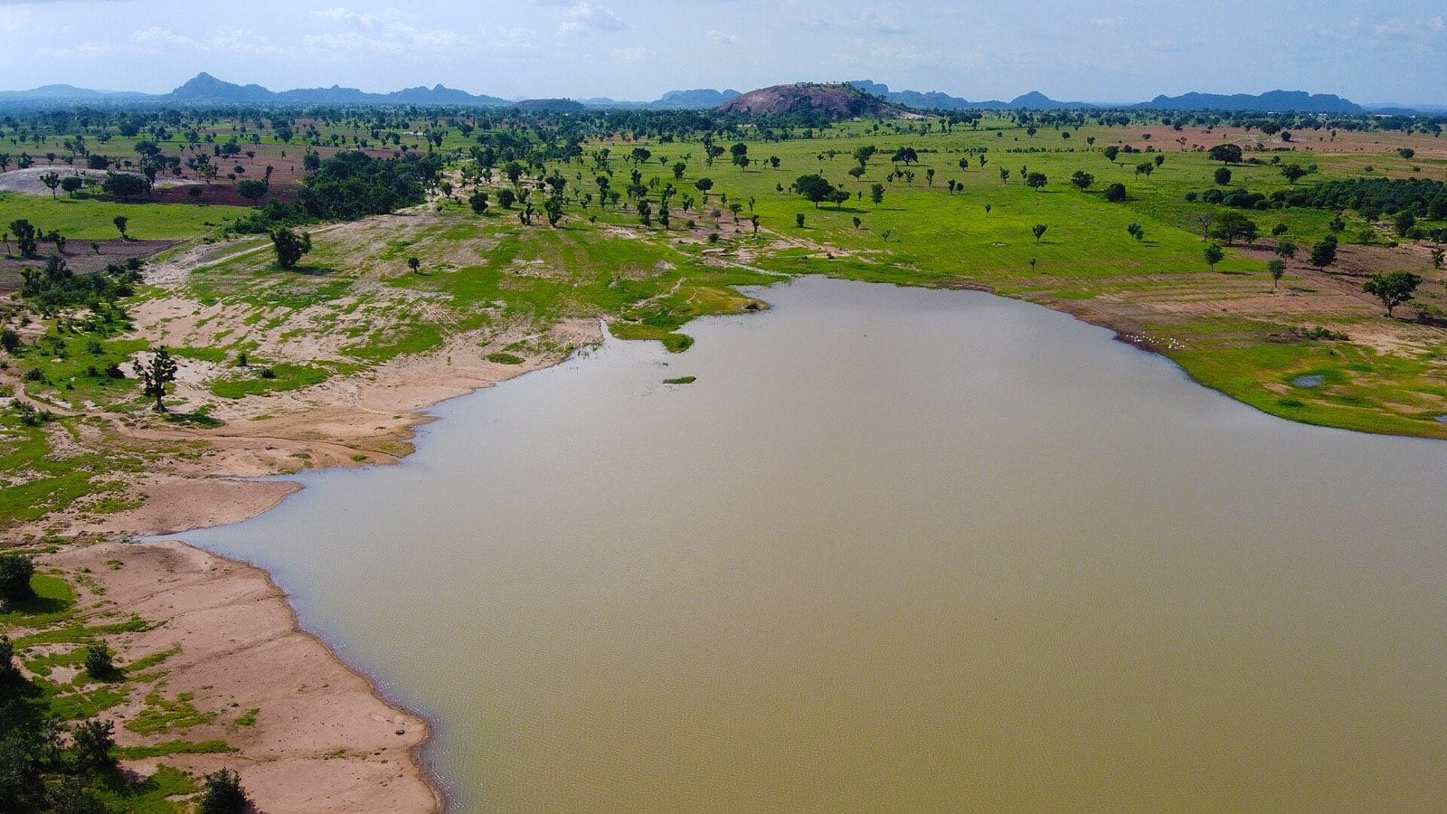 A lake lying within farmland, with hills behind it.