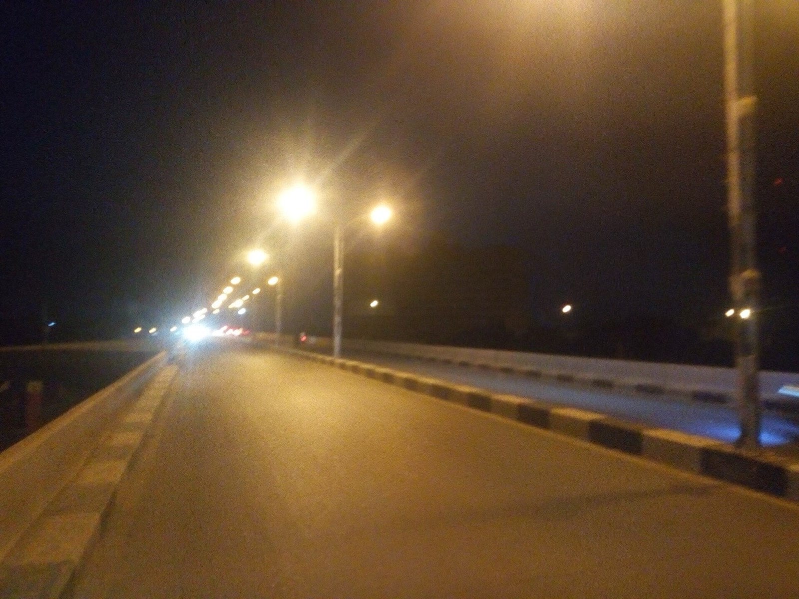 An empty city road at night under a line of streetlights.