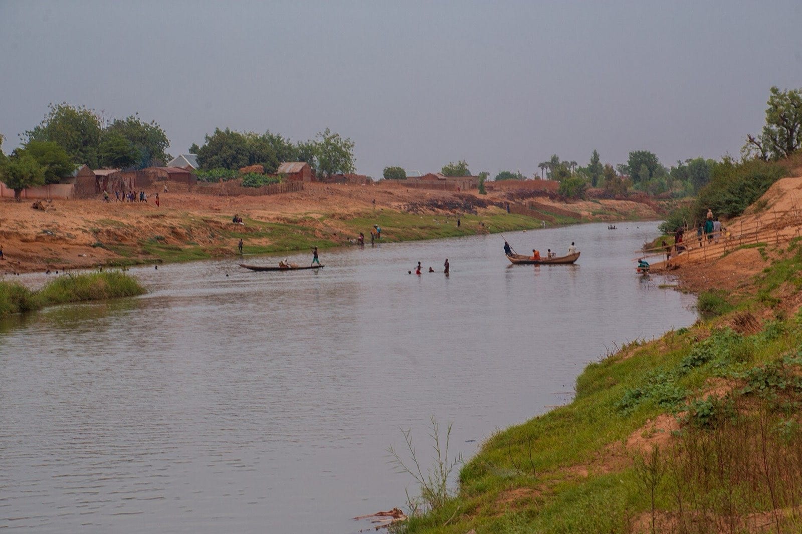 People crossing a wide river in narrow wooden boats in Kebbi State.