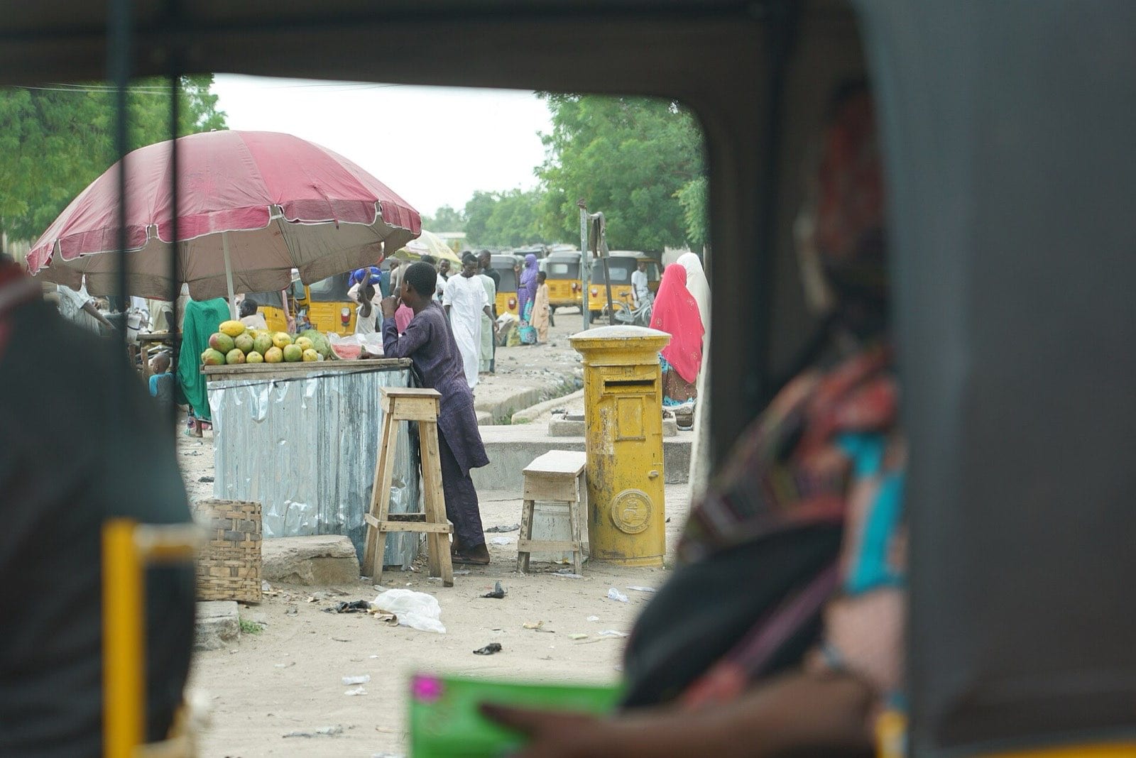 A three-wheeled keke tricycle passing a street market.